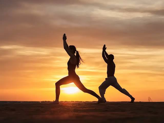 Two people practising yoga at sunset